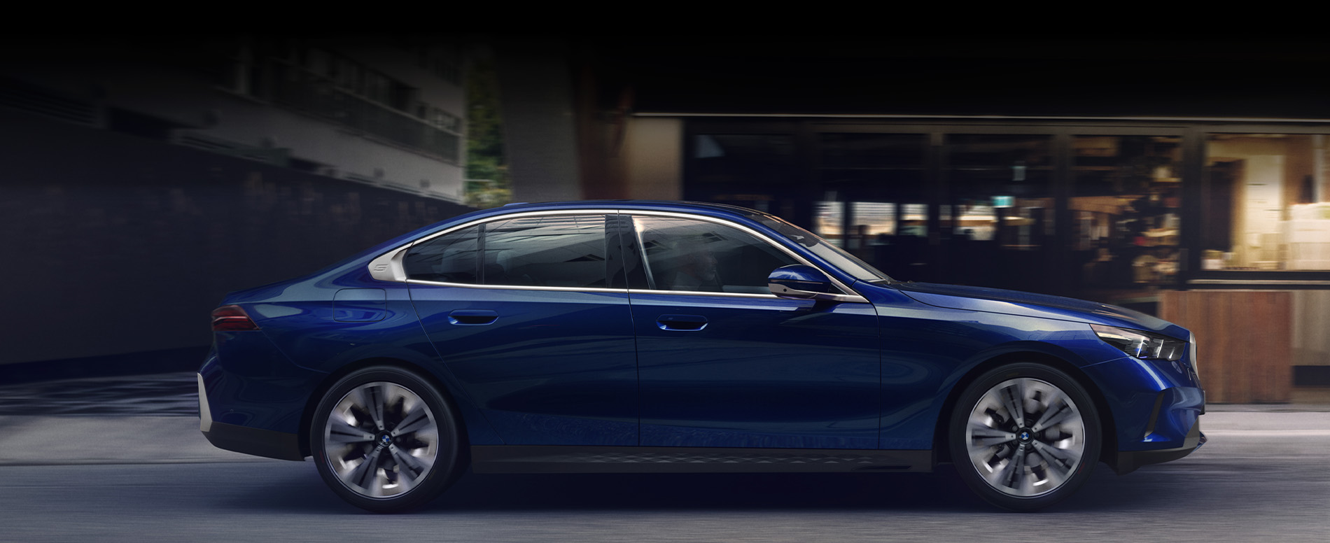 Blue BMW 5 Series driving through a city at night.