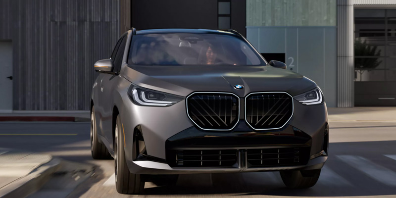 Sleek gray BMW X3 driving on a city street, showcasing its modern design and bold front grille. The scene conveys a sense of power and elegance.